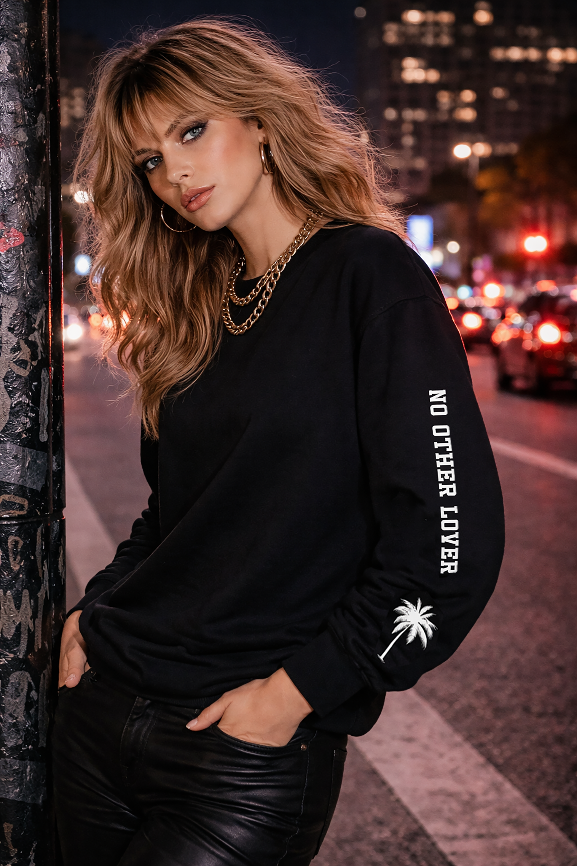 Woman wearing a black sweatshirt with text and palm tree design on a city street at night.
