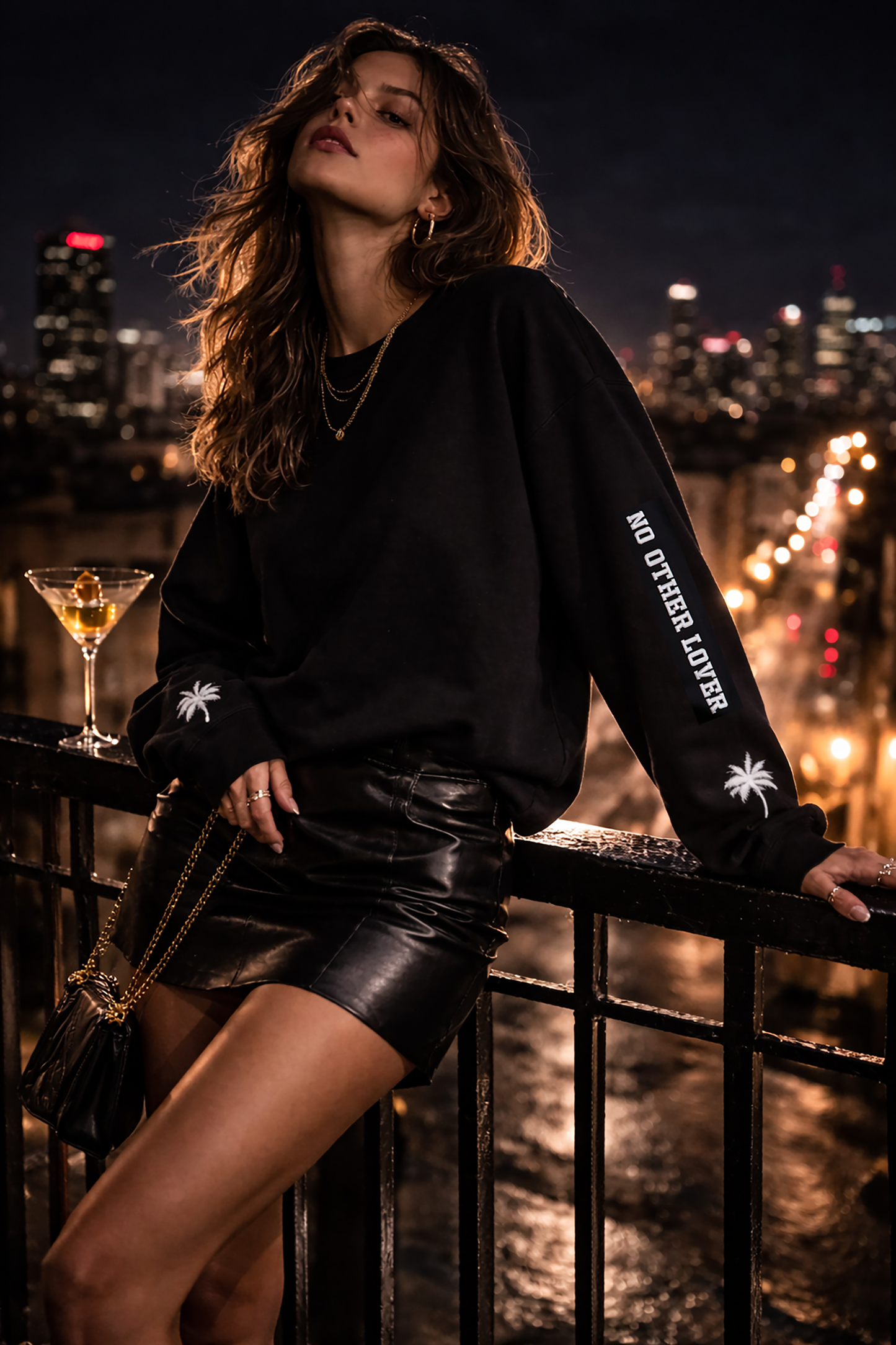 Woman in a black leather skirt with 'No Other Lover' white text and palm tree design on the sleeves, against a cityscape at night.