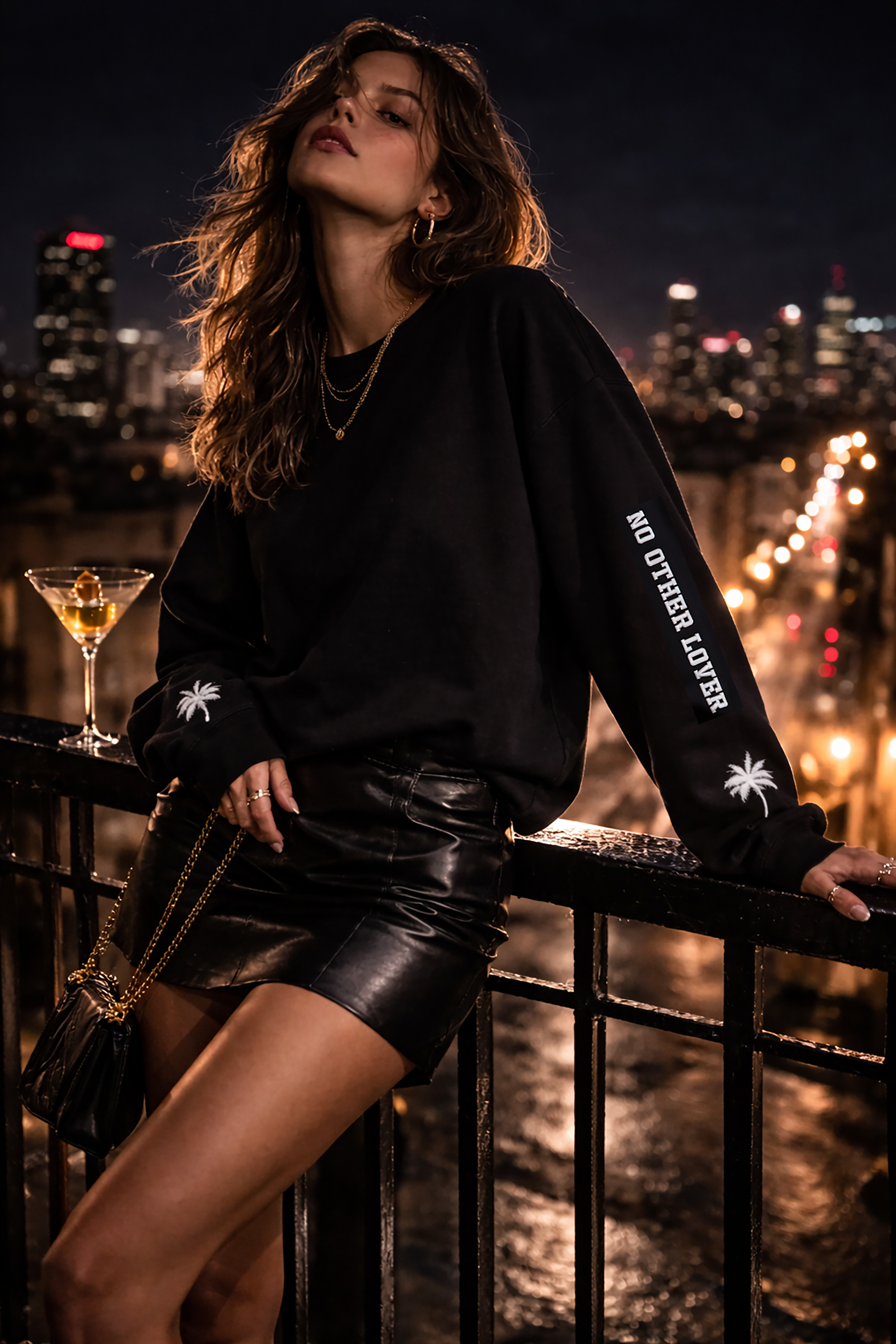 Woman in a black leather skirt with 'No Other Lover' white text and palm tree design on the sleeves, against a cityscape at night.