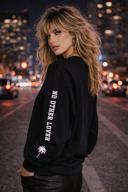 Woman with a wolf cut, wearing a black sweatshirt with text and palm tree design on a city street at night.