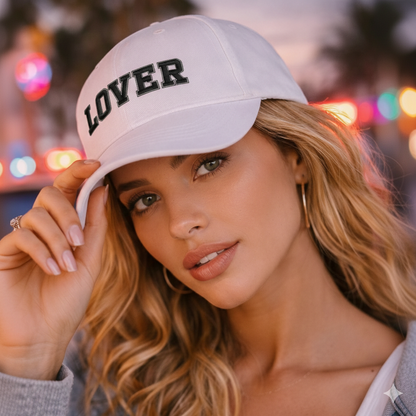 Woman wearing a white cap with 'LOVER' text against a blurred colorful background