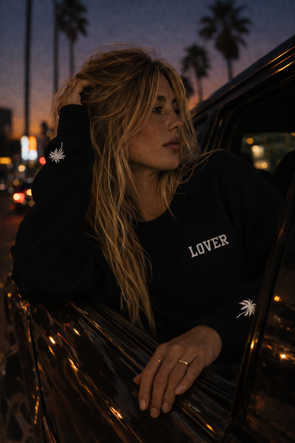 Woman wearing a black No Other Lover LOVER Palms Sweatshirt with 'LOVER' printed on it, leaning out of a car window at night.