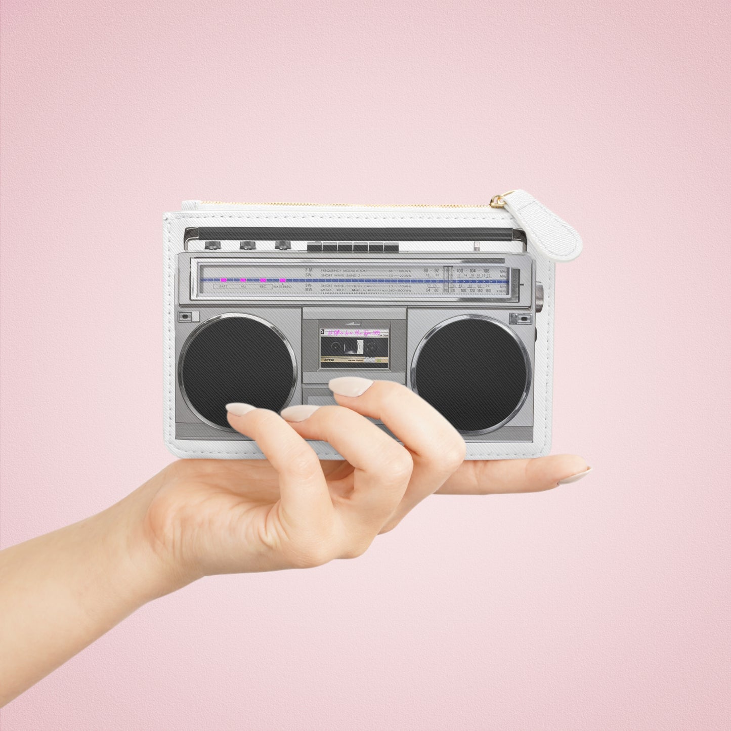 Hand holding a mini boombox-shaped purse against a pink background